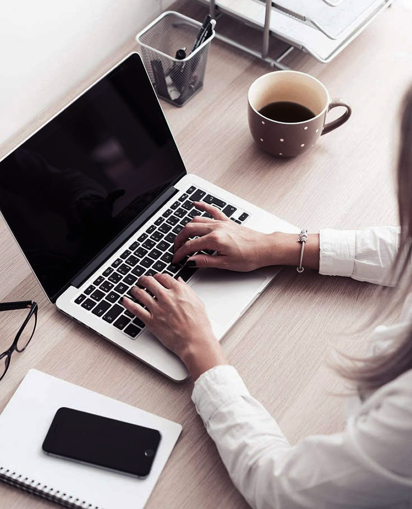 Person working on a laptop with a phone and coffee on the desk